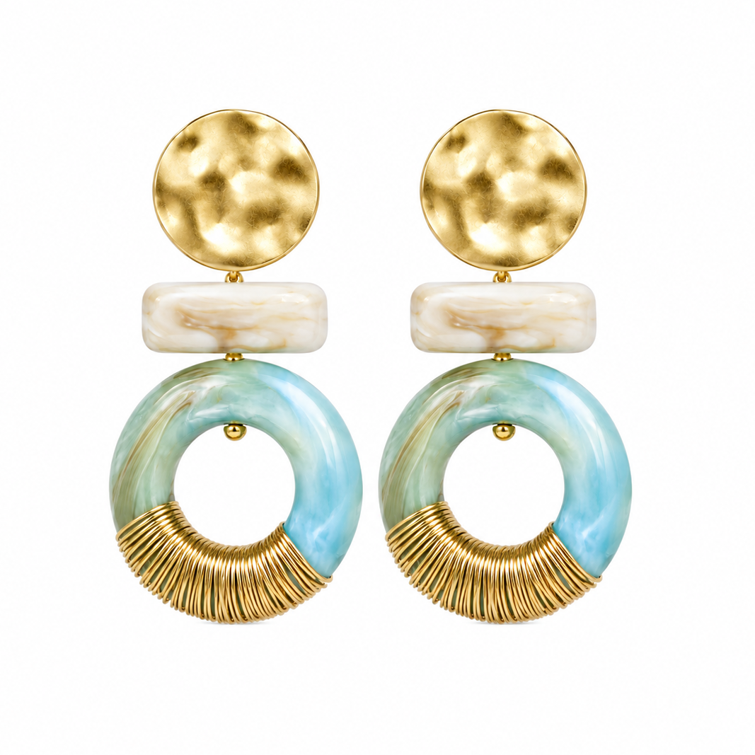 A pair of statement dangle earrings featuring hammered gold-tone circular studs, a white marbled rectangular bead, and a large circular drop in light blue and white marbled resin with a gold-tone textured lower section.